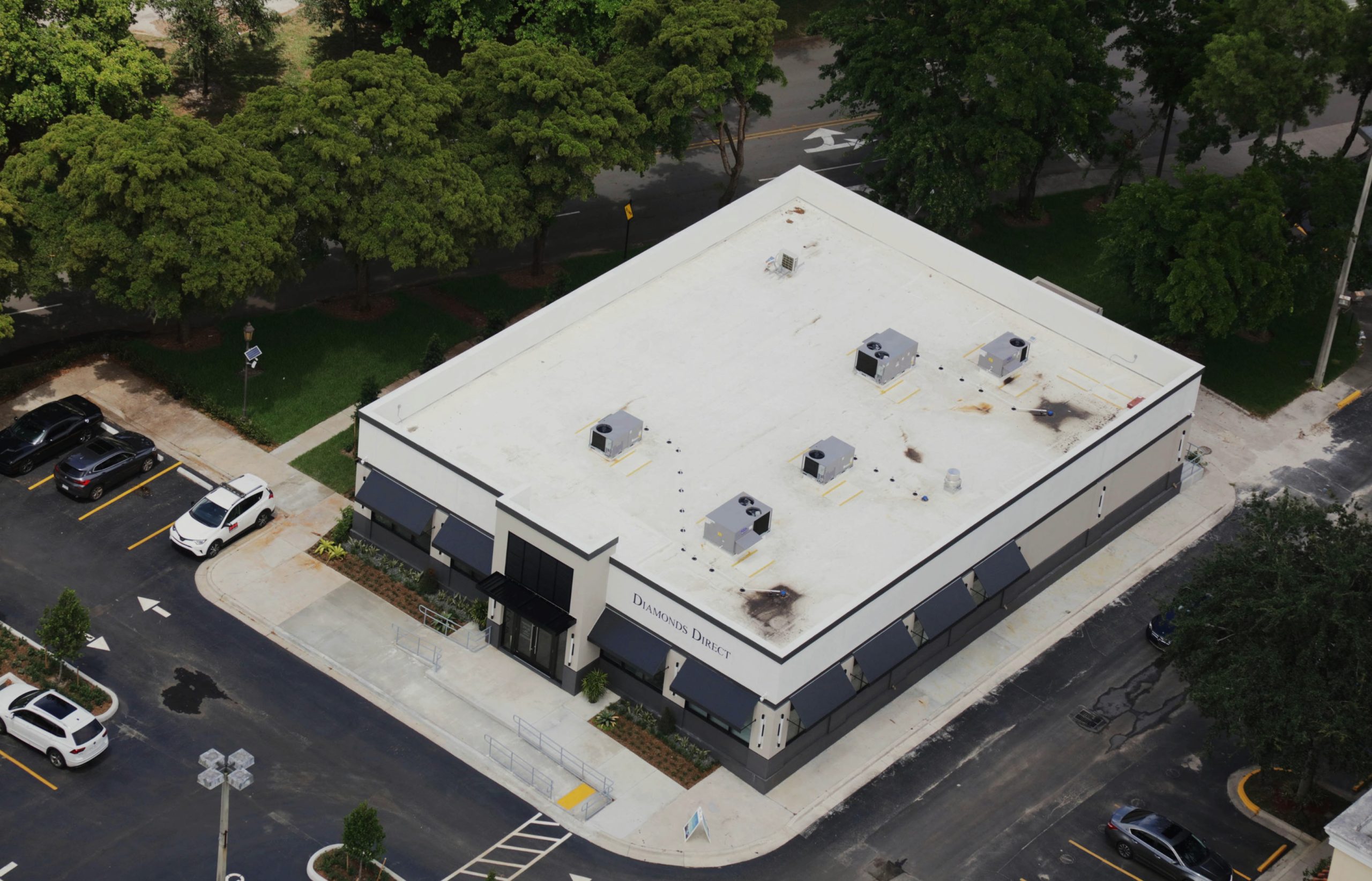 Aerial view of a Diamonds Direct store building with a white flat roof, HVAC units, storefront awnings, and a parking lot