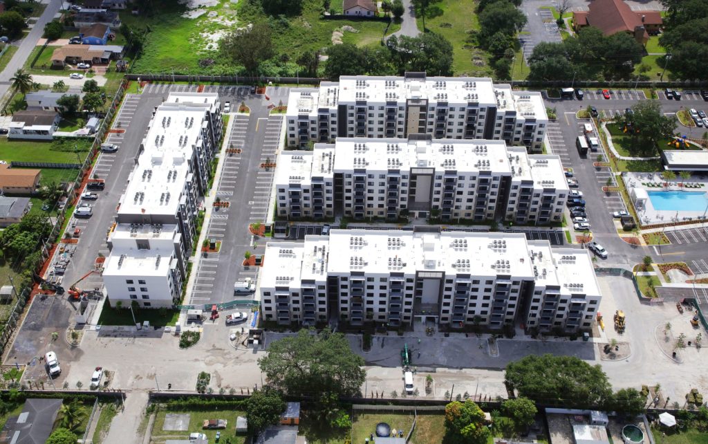 Aerial view of a large multi-building apartment complex with parking lots, pool, and surrounding neighborhood